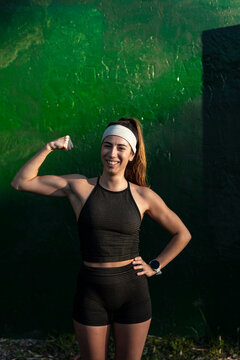 Fit athlete showing biceps against a green wall outdoors