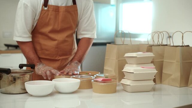 Close-up of a male chef packing freshly prepared fresh meals for online food delivery in a small business kitchen. Cloud kitchen, local restaurant, food startup. Meal prep and entrepreneur concept.
