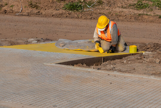 Worker squatting while painting pedestrian access ramp with yellow safety paint