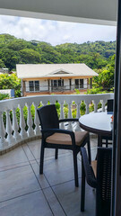 Obraz premium Empty wicker chairs wait on a shaded balcony overlooking a lush tropical hillside, framed from an open doorway with a calm mood. The scene evokes relaxed travel, outdoor living, and peaceful escapes.