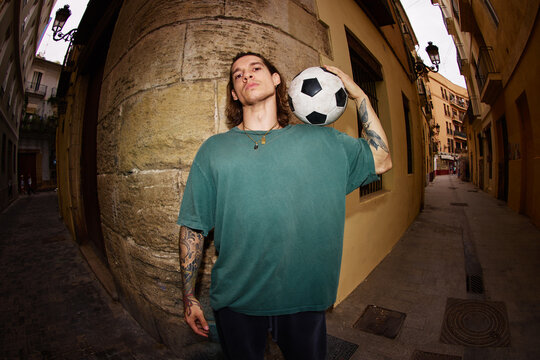 Young man holds soccer ball on narrow street in urban area