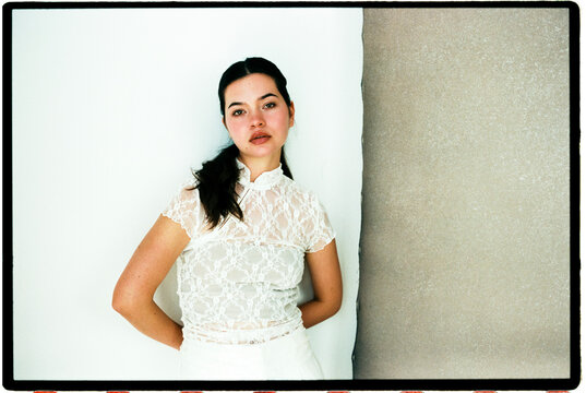 Woman posing in lace top against white wall