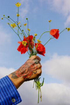 Holding flowers in hand against a blue sky with clouds
