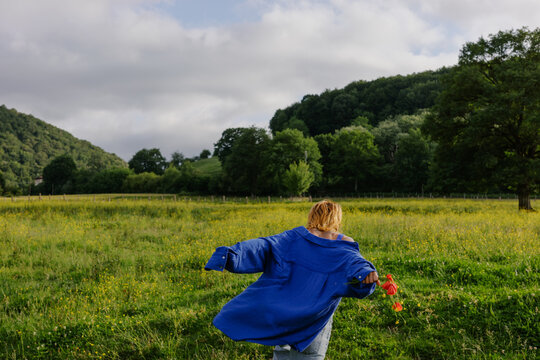 Woman runs through a green field on a cloudy day in springtime