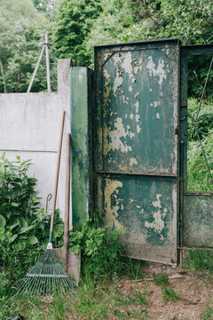 An old green gate next to a garden tool.