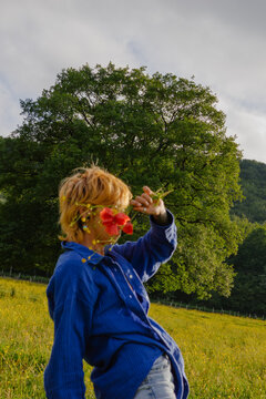 Person holding flowers in a field near a large tree in nature