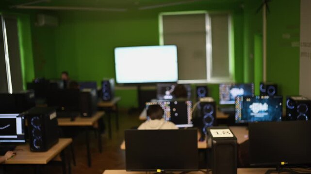 Students sitting at computers in modern classroom with green walls and large interactive whiteboard.