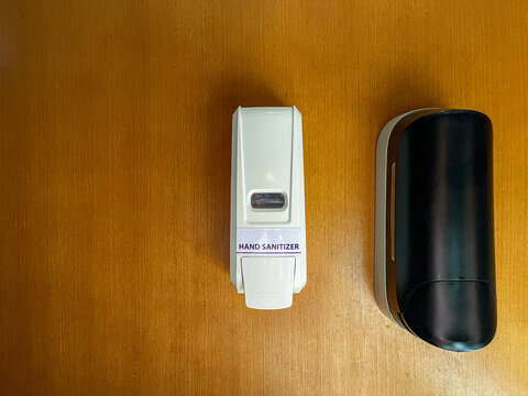Manual press hand sanitizer dispenser mounted on a wood-paneled interior wall, providing convenient hygiene access in a clean and welcoming indoor environment.