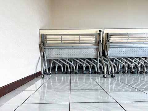Stacked folding chairs with wheels placed neatly at the corner of a room, highlighting space-saving design, mobility, and practical furniture arrangement ready for flexible use.