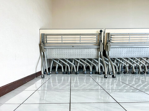 Stacked folding chairs with wheels placed neatly at the corner of a room, highlighting space-saving design, mobility, and practical furniture arrangement ready for flexible use.