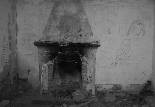 Antigua chimenea de le&ntilde;a rota y abandonada en el interior de una casa en ruinas con paredes llenas de grafitis y pintadas en blanco y negro