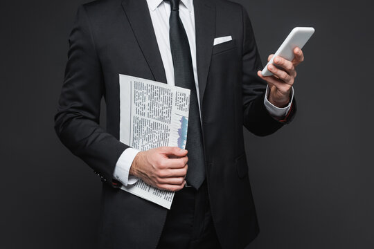 Charming gentleman dressed elegantly checks news on phone while holding newspaper