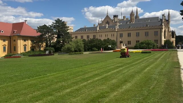 Ride on lawn mower maintains the formal gardens of Lednice Castle in the Czech Republic on a sunny summer day. Historic palace, landscape maintenance, cultural heritage, tourism and European travel.