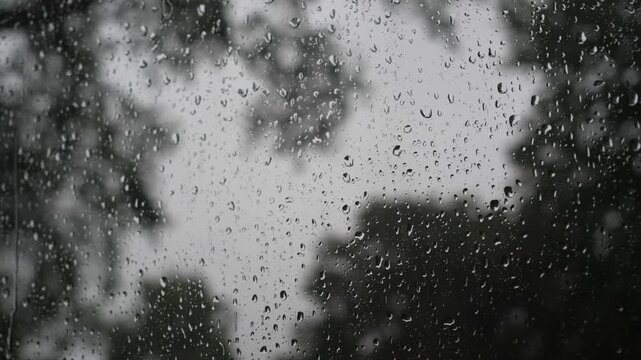 Close up macro view of rain drops sliding and trickling down a glass window pane on a rainy day, with a soft blurred background creating a calm and moody atmosphere.