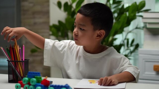 Focused child draws with crayon at home. Colorful pencils and blocks nearby. Child concentrates on creative activity. Ideal for education, parenting, childhood themes. Natural light, cozy background.
