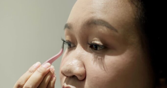 Close-up of young Asian woman putting on false eyelashes