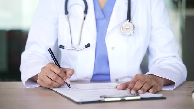 Close up of female doctor signing medical documents while sitting at desk in modern clinic. Healthcare professional completes paperwork, approves records and finalizes patient prescription.