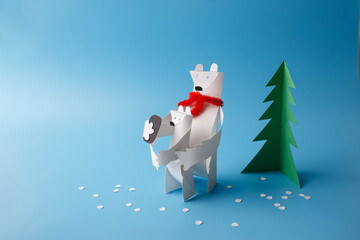Paper polar bear holding polar bear cub beside paper fir tree on blue background with paper snow. Family care and Christmas concept. Design for postcard. Front view with copy space, © Elena