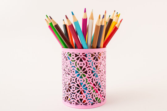 The pink cup with colored wooden crayons on the white background. Back to school idea.