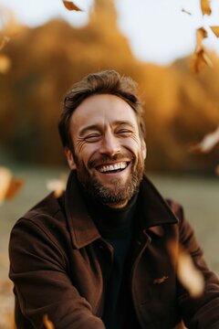 Bearded man laughing outdoors with autumn leaves falling for lifestyle portrait and seasonal banner or social media use