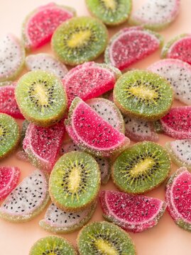 Assorted colorful fruit flavored gummy candies shaped like kiwi and watermelon slices on a light background