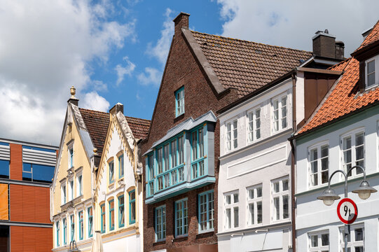 Historic gabled houses and restored facades at the harbor of Husum beneath a blue summer sky with white clouds.