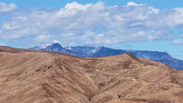 Aerial of arid mountain landscape with dirt road and distant snow capped Stuart Range peaks in Wenatchee Washington