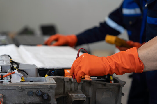 High-voltage battery checks, and maintenance. Technician or Mechanic wearing protective gloves diagnosing electric car vehicles battery, component checks at auto workshop