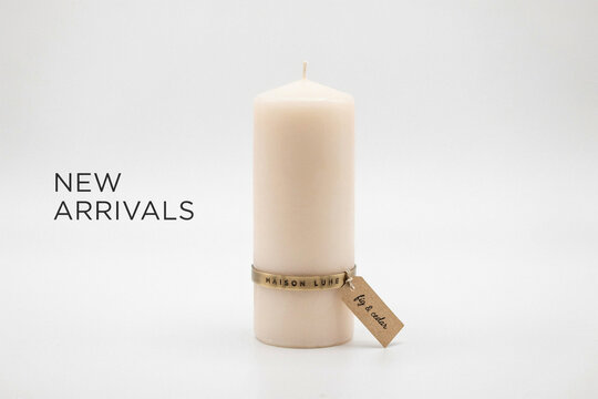 A single elegant unlit light peach pillar candle stands upright adorned with a decorative brass band featuring the stamped name Maison Lune and a small brown tag indicating a fig and cedar scent