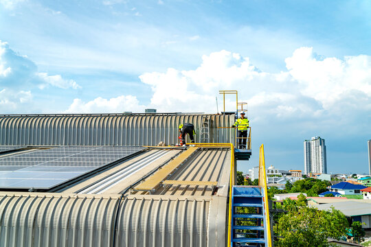Workers repair roof near a city with tall buildings under a clear sky with clouds