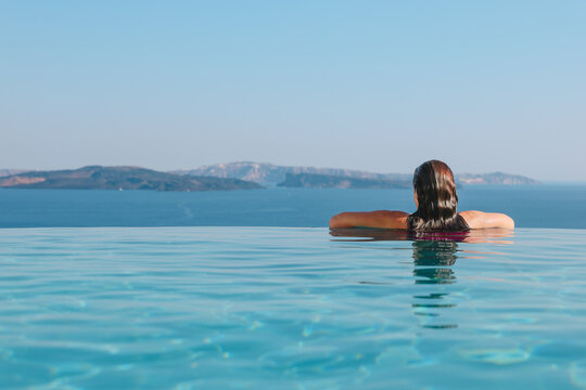 A woman rests at the edge of an infinity pool overlooking the Aegean Sea in Santorini, Greece &mdash; a tranquil scene of Mediterranean luxury.