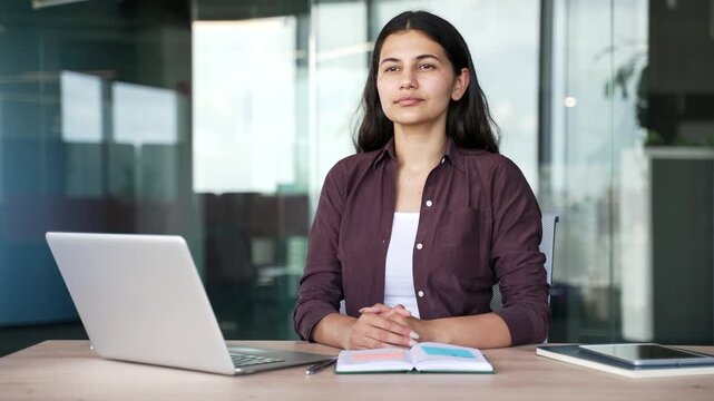 Female office worker takes a mindful breathing break during workday in modern business office. Calm businesswoman inhales and exhales slowly, reducing tension and improving mental health.