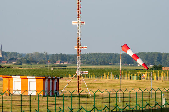 A red and white antenna mast a windsock and runway markers stand along the grassy perimeter of Brussels Airport in Belgium at golden hour.