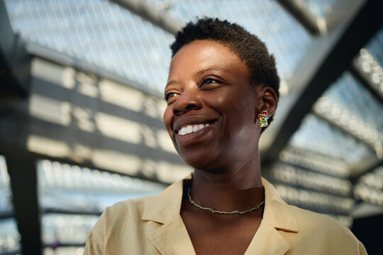 Close up of young adult Black woman smiling and looking away in modern workplace, conveying confidence and leadership. Ideal for diversity hiring, career growth, corporate branding