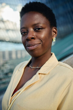Vertical portrait of young adult Black woman looking at camera and smiling, conveying confidence and professional identity. Useful for leadership, career growth, diversity marketing