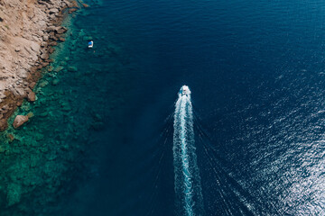 Aerial view of a fast motor yacht cutting through crystal-clear blue water. Vibrant textures, dynamic waves, powerful motion create the perfect visual for themes of luxury, freedom, vacation. © Miha Creative