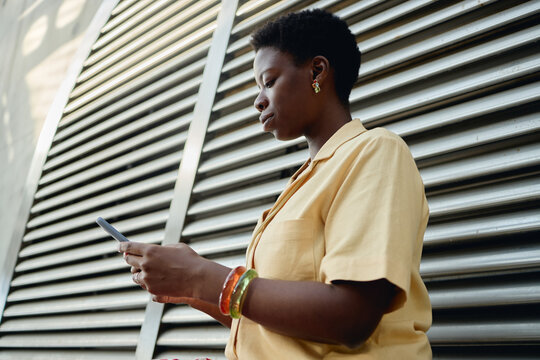 Young adult African American woman checking smartphone outdoors, managing mobile communication and digital tasks. Useful for remote work, messaging, fintech, social media marketing