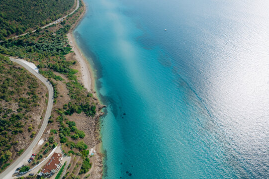 Aerial drone of a peaceful beach in Thassos, Greece, featuring transparent turquoise water, paddleboards, swimmers and a beautiful Mediterranean coastline.