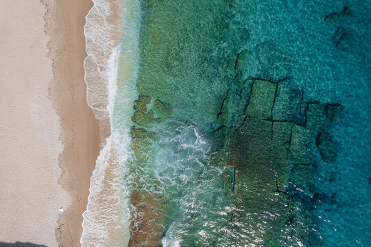 Aerial drone of a peaceful beach in Thassos, Greece, featuring transparent turquoise water, paddleboards, swimmers and a beautiful Mediterranean coastline.