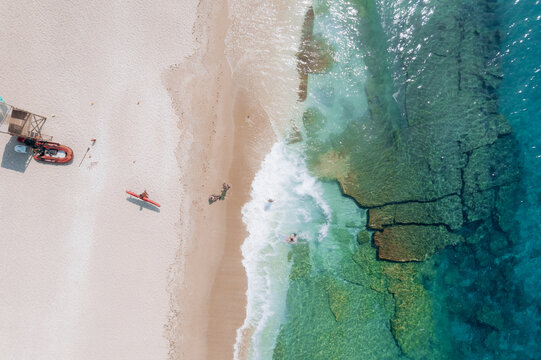 Aerial summer landscape of a turquoise lagoon on Thassos Island, Greece, showing crystal clear water, beach, swimmers, paddleboards and rocky coastline.