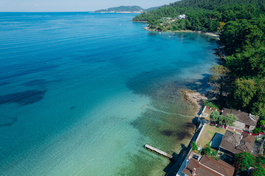 Aerial summer landscape of a turquoise lagoon on Thassos Island, Greece, showing crystal clear water, beach, swimmers, paddleboards and rocky coastline.