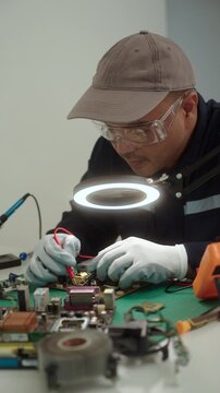 Close-up technician repairing a printed circuit board in a modern repair lab. PCB diagnostics, soldering electronic maintenance, right to repair. Sustainable technology and skilled technician.

