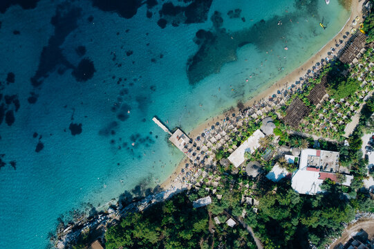 Aerial drone of a peaceful beach in Thassos, Greece, featuring transparent turquoise water, paddleboards, swimmers and a beautiful Mediterranean coastline.