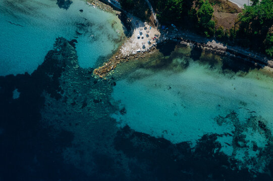 Aerial drone of a peaceful beach in Thassos, Greece, featuring transparent turquoise water, paddleboards, swimmers and a beautiful Mediterranean coastline.
