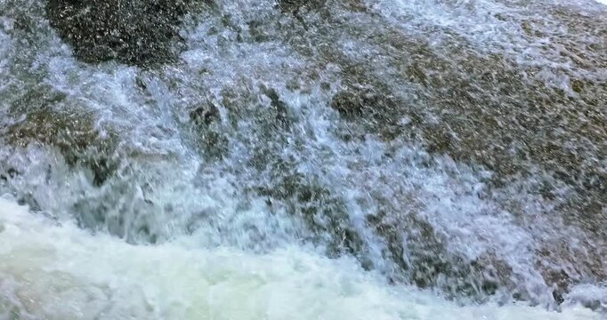 Close up view of splashing water over rock in mountain stream, creating natural texture and rapid movement.