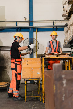 Two factory technicians inspecting metal strip beside power press machine supporting efficient production and workplace safety inside a busy metalworking factory setting