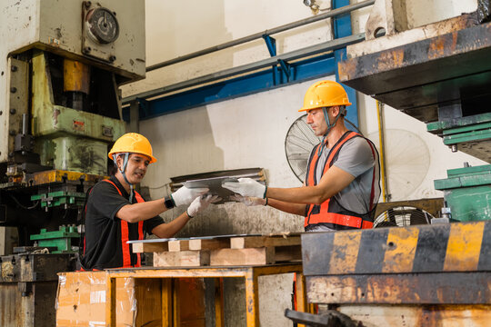 Coworkers passing stamped sheet metal panel beside mechanical power press machine