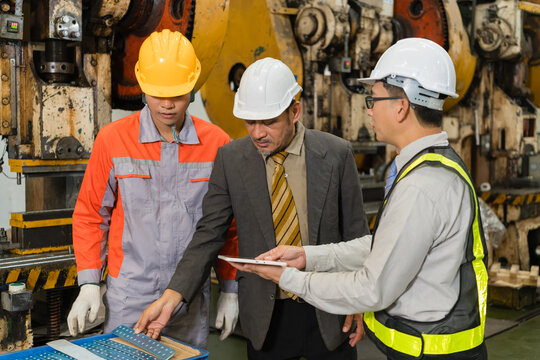 Manager and engineer study a tablet screen as a young worker sorts stamped parts amid old power presses