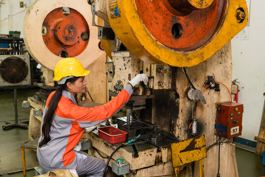 Female machine operator adjusting die on power press in metal stamping factory