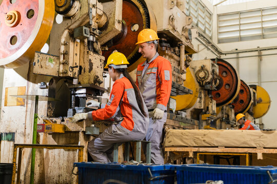 Supervisor observing female technician operating punch press die in metal stamping workshop